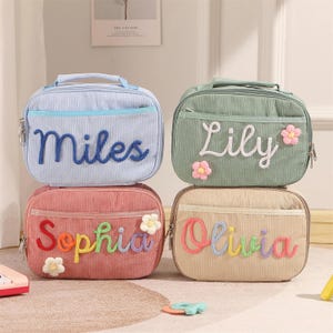 May include: Four rectangular corduroy pouches with top handles and zippered closures. The light blue pouch features the name Miles, the green pouch says Lily with flower accents, the pink pouch says Sophia, and the beige pouch says Olivia.