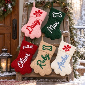 May include: Five paw-shaped knit Christmas stockings in pink, dark green, red, beige, and cream. Each features a cuff with a stitched icon&mdash;a paw print, bone, or cat face&mdash;and a personalized name embroidered in cursive: Daisy, Max, Oliver, Ruby, and Archie.