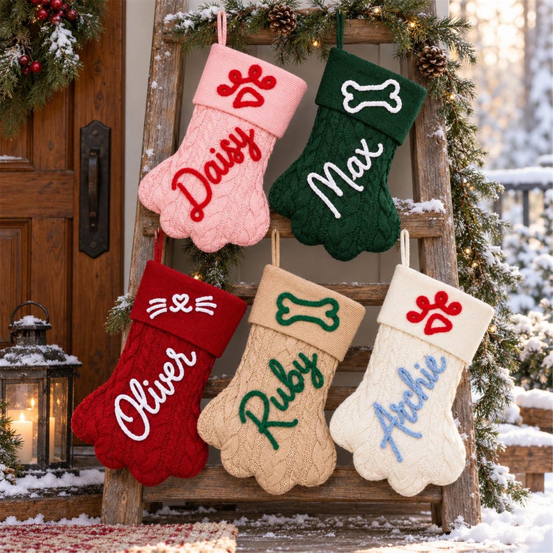 May include: Five paw-shaped knit Christmas stockings in pink, dark green, red, beige, and cream. Each features a cuff with a stitched icon&mdash;a paw print, bone, or cat face&mdash;and a personalized name embroidered in cursive: Daisy, Max, Oliver, Ruby, and Archie.