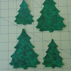 May include: Four green felt Christmas tree shapes of varying sizes. The trees are cut out and have a speckled texture.