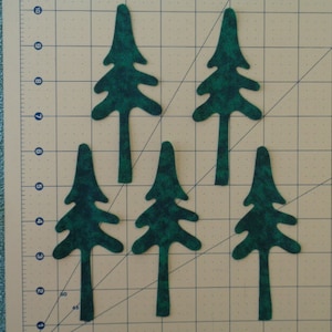 May include: Five green felt Christmas tree shapes on a beige self-healing cutting mat. The trees are all the same size and shape, and they are arranged in a staggered pattern.