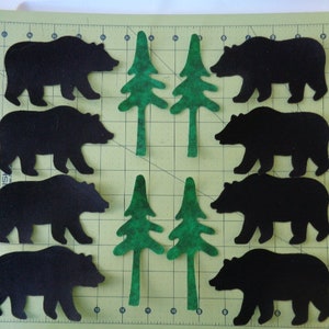May include: Eight black felt bear silhouettes and four green felt pine tree silhouettes on a green cutting mat.