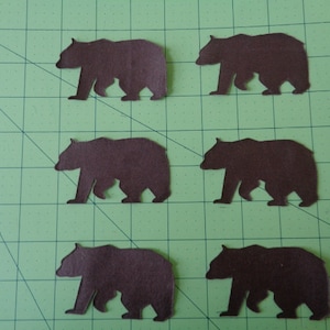 May include: Six brown paper bear cutouts on a green grid background.