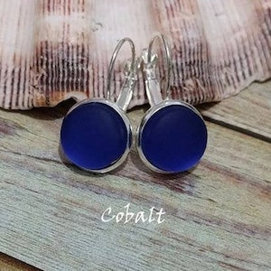 May include: Cobalt blue glass earrings with silver hoops. The earrings are round and have a smooth, frosted finish.