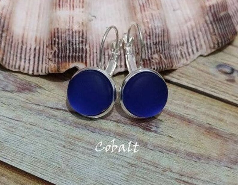 May include: Cobalt blue glass earrings with silver hoops. The earrings are round and have a smooth, frosted finish.