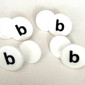 May include: Six white round plastic tiles with the letter "b" printed in black on each tile.