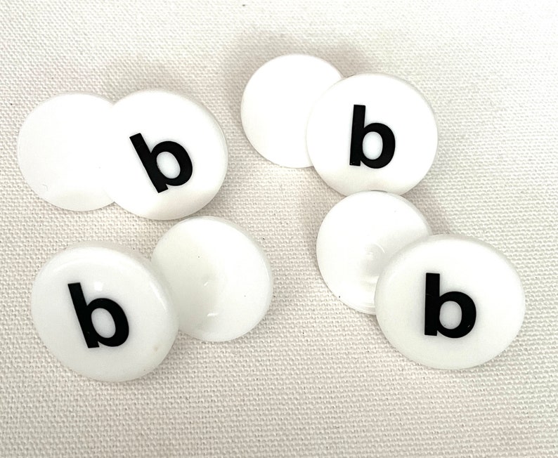 May include: Six white round plastic tiles with the letter "b" printed in black on each tile.