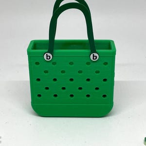 May include: A green tote bag with a green handle and two white "b" letters on the front. The bag has a pattern of small holes.