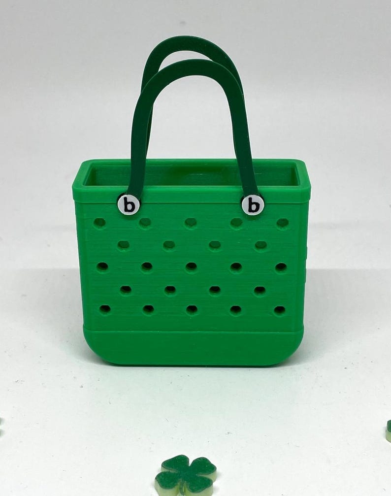 May include: A green tote bag with a green handle and two white "b" letters on the front. The bag has a pattern of small holes.