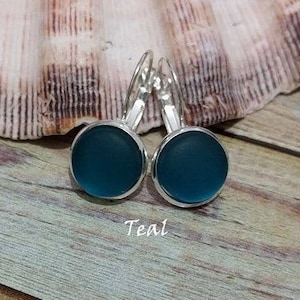 May include: Teal glass earrings with silver hooks. The earrings are round and have a smooth, glossy finish.