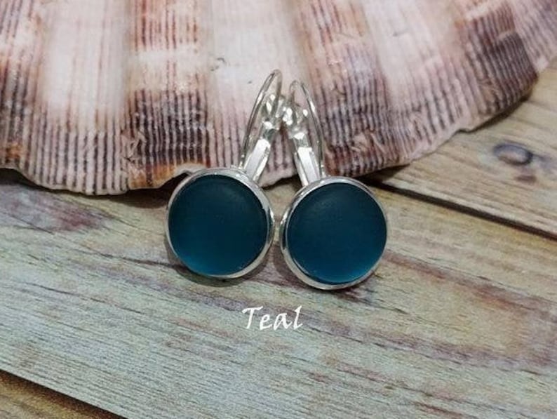 May include: Teal glass earrings with silver hooks. The earrings are round and have a smooth, glossy finish.