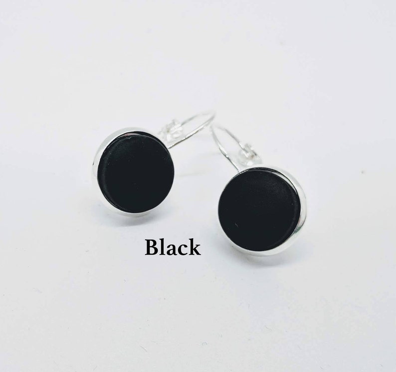May include: A pair of silver dangle earrings with black round cabochon stones. The earrings are labeled "Black".