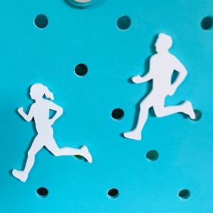 May include: Two white silhouette figures of runners on a light blue background. The figures are cut out and attached to the surface.