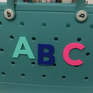 May include: A teal blue tote bag with the letters A, B, and C in different colors. The letter A is turquoise, the letter B is dark blue, and the letter C is pink.