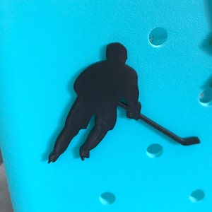 May include: Black silhouette of a hockey player skating and holding a stick on a turquoise background.