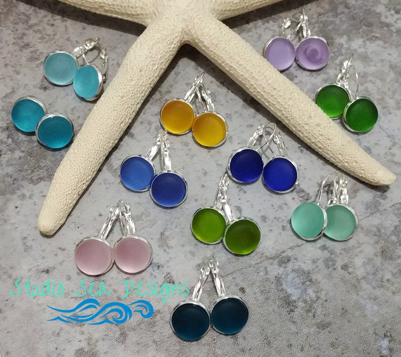 May include: Assortment of colorful glass earrings with silver hoops. The earrings are displayed on a white starfish and a gray surface.
