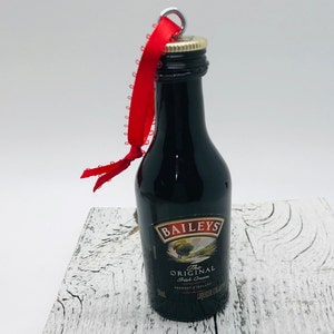 May include: A miniature bottle of Baileys Irish Cream liqueur with a red ribbon attached. The bottle is a Christmas ornament.