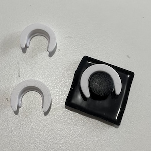May include: Three white plastic rings, two are laying flat and one is attached to a black square with a black round button in the center.