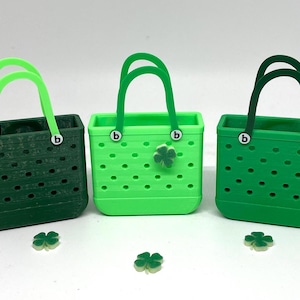 May include: Three green tote bags with a clover charm. The bags are made of a textured material with small holes. The bags have a white "b" on each side.
