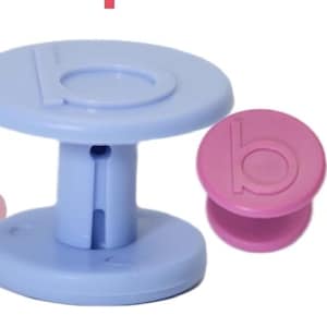 May include: A collection of colorful, plastic objects in shades of pink and blue. The objects include a small, pink spool-shaped item, a larger blue table-like structure, and two round, button-like items in pink and lavender. Each item has a letter "b" on it.