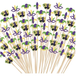 May include: A collection of Mardi Gras-themed party picks. Each pick features a decorative cutout in the shape of a mask, jester hat, fleur-de-lis, or comedy/tragedy masks in purple, green, and yellow. The picks are made of wood.