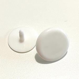 May include: Two white plastic buttons with a small raised nub on one button. The buttons are round and smooth.