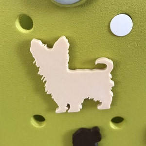 May include: A white plastic cutout of a Yorkshire Terrier dog on a green background.