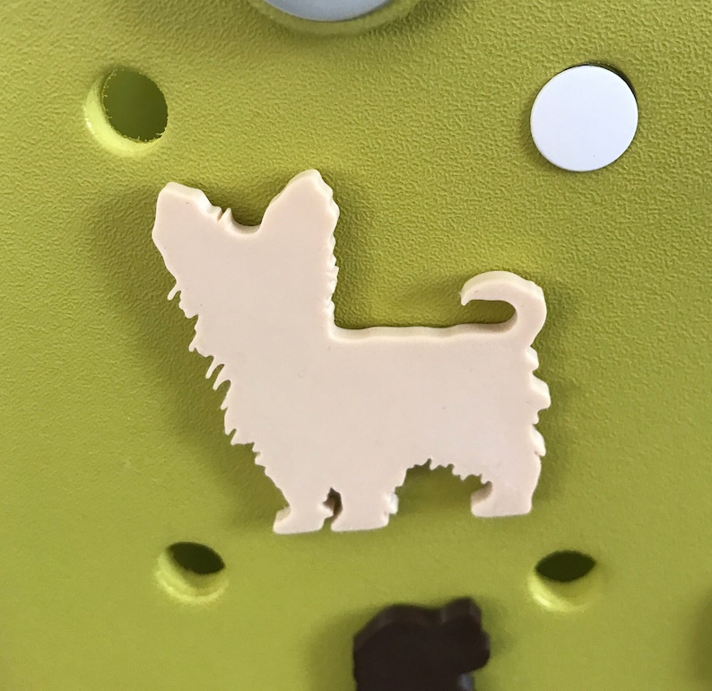 May include: A white plastic cutout of a Yorkshire Terrier dog on a green background.