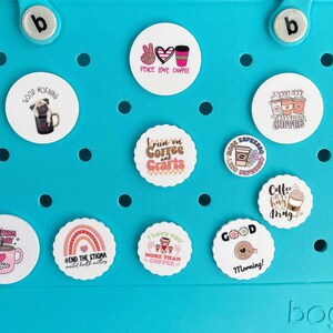 May include: A blue plastic storage container with various round stickers featuring coffee-themed designs and text. The stickers include phrases like "Peace Love Coffee", "Good Morning", "Run on Coffee and Crafts", "Coffee is my Drug", and "I Love You More Than Coffee".