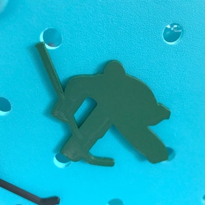 May include: A green plastic silhouette of a hockey player holding a stick, on a blue background.