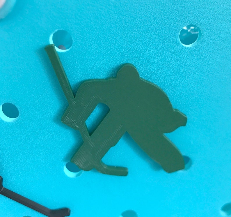 May include: A green plastic silhouette of a hockey player holding a stick, on a blue background.