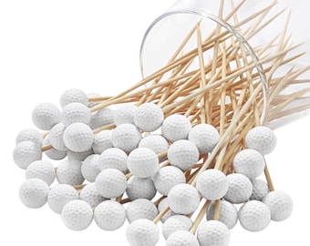 Op de afbeelding: Een verzameling houten tandenstokers, elk bekroond met een klein wit bolletje met een kuiltjesstructuur die lijkt op een golfbal. De tandenstokers vallen uit een doorzichtige glazen houder en vormen een cluster van decoratieve prikkers.
