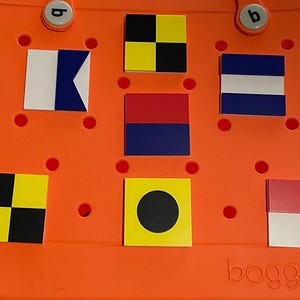 May include: A bright orange plastic tote bag with the word "BOGG" printed on the bottom. The bag has a variety of colorful square patches attached to it, including black and yellow checkered, red and blue, and a black circle on a yellow background.