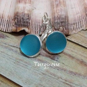 May include: A pair of turquoise blue glass earrings with silver hooks. The earrings are oval shaped and have a smooth, polished finish.
