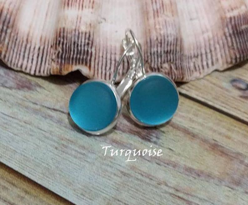 May include: A pair of turquoise blue glass earrings with silver hooks. The earrings are oval shaped and have a smooth, polished finish.