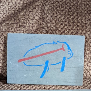 May include: A blue and red painted wooden sign with a stylized buffalo silhouette.