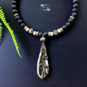 May include: A black lava rock and white bead necklace with a gold pendant featuring a brown agate stone with a gold snake design.