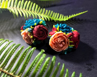 Op de afbeelding: Een paar handgemaakte polymer clay oorbellen met een cluster van kleurrijke bloemen. De oorbellen zijn gemaakt in tinten rood, roze, blauw en groen.