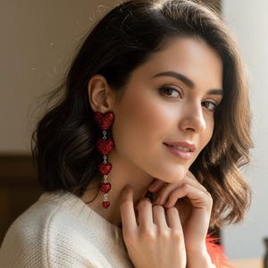May include: Red heart-shaped drop earrings. These earrings feature a cascade of glittery red hearts, diminishing in size, linked by fine chains. The earrings are a striking red and designed to be a statement piece.