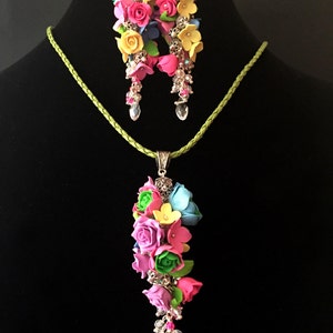 Peut inclure: Un ensemble de boucles d'oreilles florales et un collier avec un pendentif repr&eacute;sentant un bouquet de fleurs color&eacute;es. Les fleurs sont en p&acirc;te polym&egrave;re et sont dans des tons de rose, jaune, bleu et vert. Les boucles d'oreilles et le collier sont rehauss&eacute;s de m&eacute;tal argent&eacute; et de cristaux transparents.