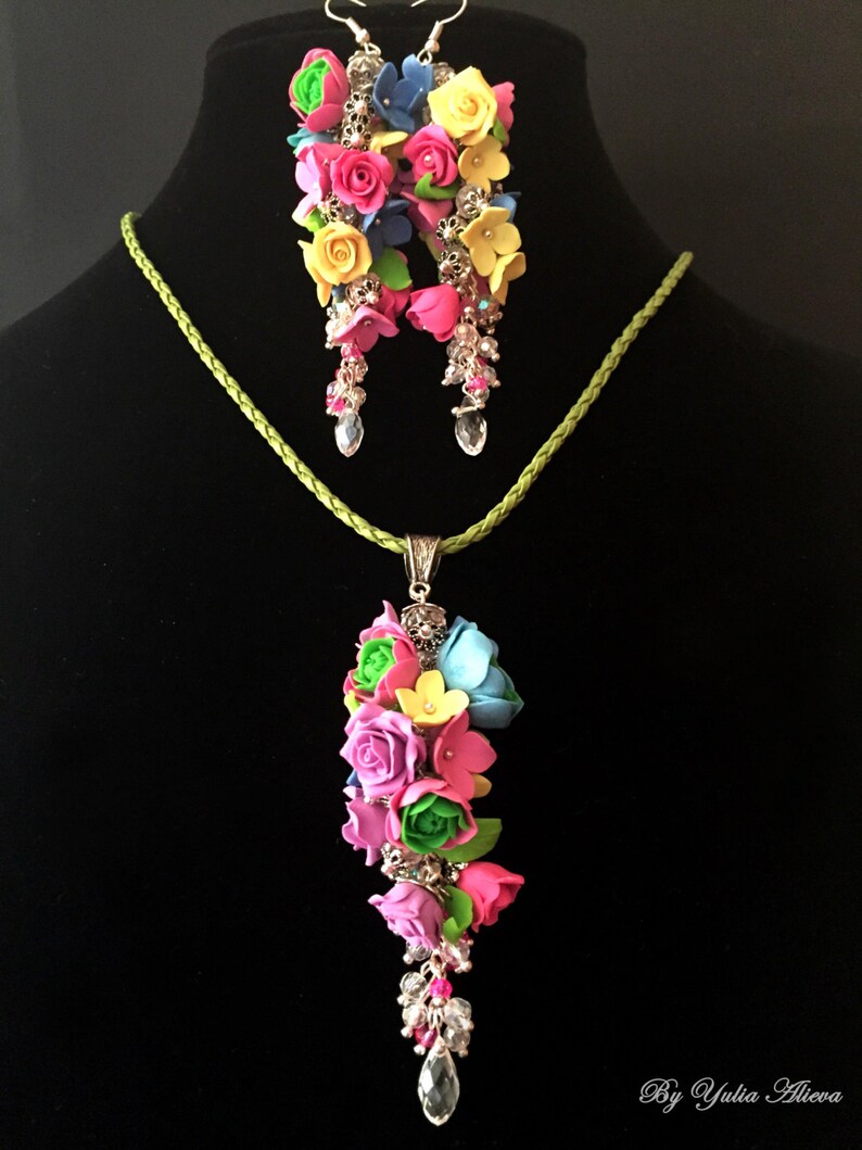 Peut inclure: Un ensemble de boucles d'oreilles florales et un collier avec un pendentif repr&eacute;sentant un bouquet de fleurs color&eacute;es. Les fleurs sont en p&acirc;te polym&egrave;re et sont dans des tons de rose, jaune, bleu et vert. Les boucles d'oreilles et le collier sont rehauss&eacute;s de m&eacute;tal argent&eacute; et de cristaux transparents.