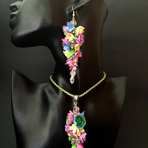 Peut inclure: Un ensemble de collier et boucles d'oreilles fleuries color&eacute;es avec un cordon vert et des accents argent&eacute;s. Les fleurs sont en p&acirc;te polym&egrave;re et sont dans des tons de rose, bleu, jaune et vert.
