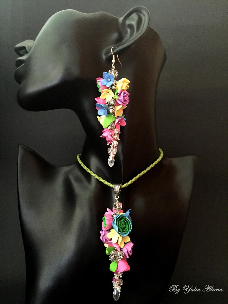 Peut inclure: Un ensemble de collier et boucles d'oreilles fleuries color&eacute;es avec un cordon vert et des accents argent&eacute;s. Les fleurs sont en p&acirc;te polym&egrave;re et sont dans des tons de rose, bleu, jaune et vert.