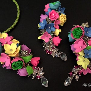 Peut inclure: Un collier et des boucles d'oreilles assortis de fleurs color&eacute;es, avec des fleurs roses, jaunes, bleues et vertes. Le collier a une cha&icirc;ne argent&eacute;e et les boucles d'oreilles ont des crochets argent&eacute;s.