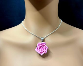 Può includere: Una collana con catena d'argento con un ciondolo a forma di rosa rosa. La rosa è realizzata in argilla polimerica e ha un aspetto realistico.