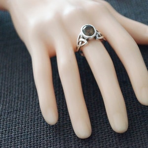 May include: A silver ring with a dark grey gemstone set in a Celtic knot design.