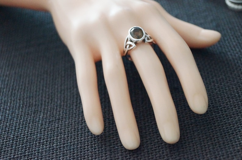 May include: A silver ring with a dark grey gemstone set in a Celtic knot design.