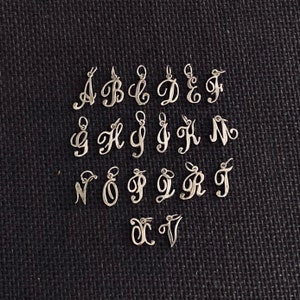 May include: A set of 26 silver charm pendants, each featuring a different letter of the alphabet in a cursive script style.