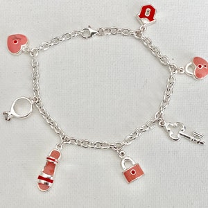 May include: A silver charm bracelet with pink and red enamel charms, including a heart, a lock, a key, a sandal, and a ring.