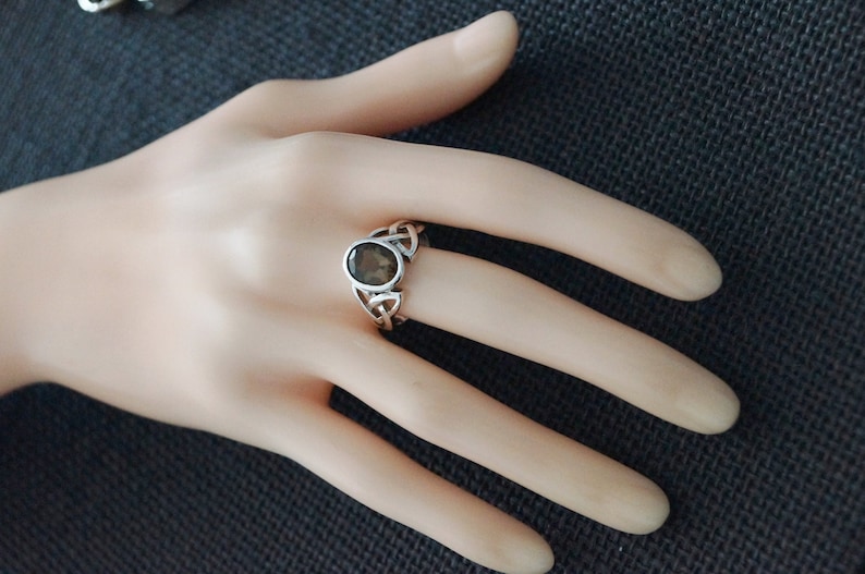 May include: A silver ring with a dark gray oval gemstone set in a Celtic knot design.